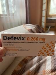 Jaukioje miegamojo aplinkoje su lova ir langu fone ranka laiko "Defevix" 0,266 mg kapsulių dėžutę.